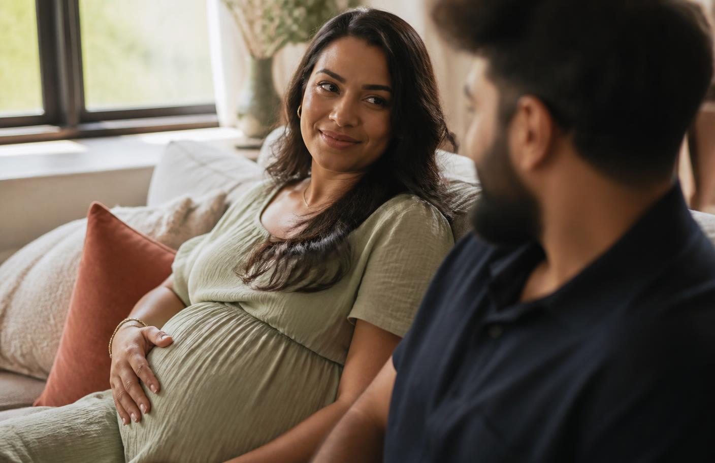Gestante sentada à mesa com frutas, legumes e uma refeição preparada em casa